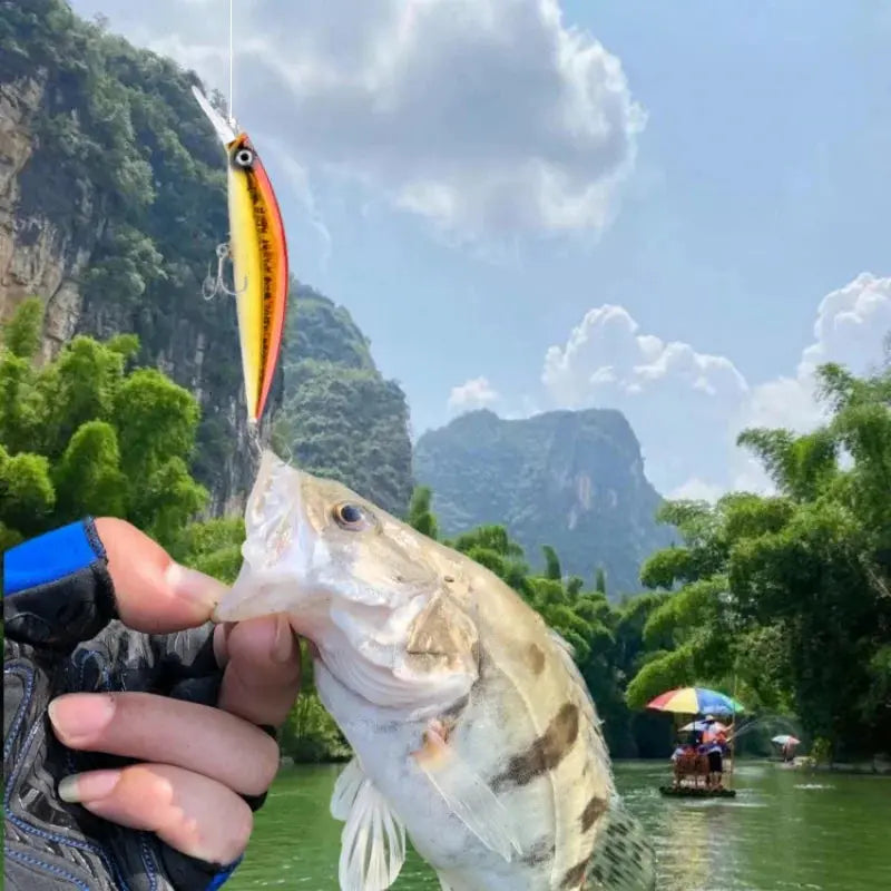 Fishing lure held by a hand with a fish caught on a mountainous river background